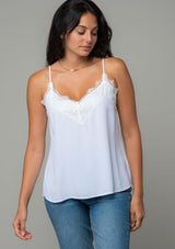 [Color: Chalk] A half body front facing image of a brunette model wearing a white lace trim camisole with a v neckline, adjustable spaghetti straps, and a flowy relaxed fit. 
