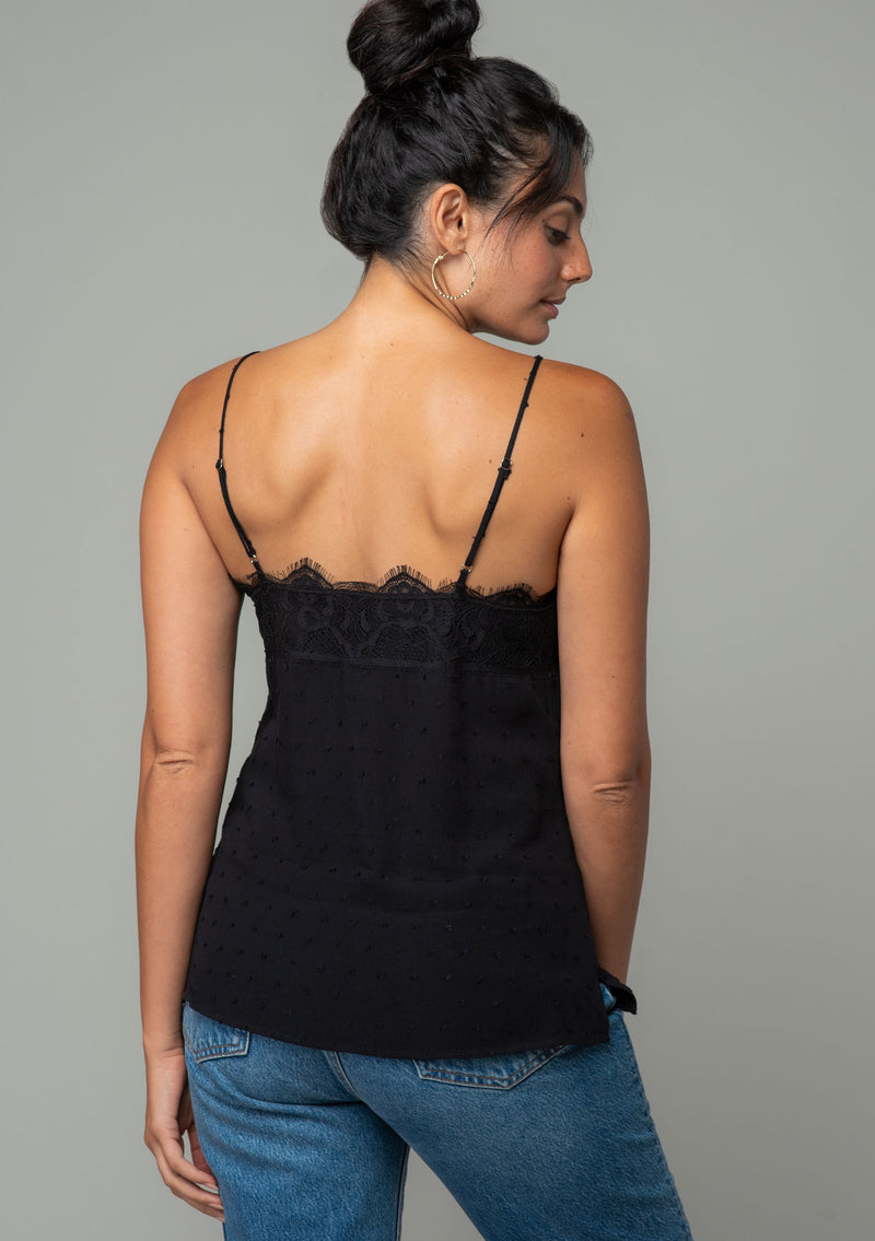 [Color: Black] A back facing image of a brunette model wearing a black clip dot camisole with a lace trim v neckline and adjustable spaghetti straps. 