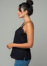 [Color: Black] A side facing image of a brunette model wearing a black clip dot camisole with a lace trim v neckline and adjustable spaghetti straps. 