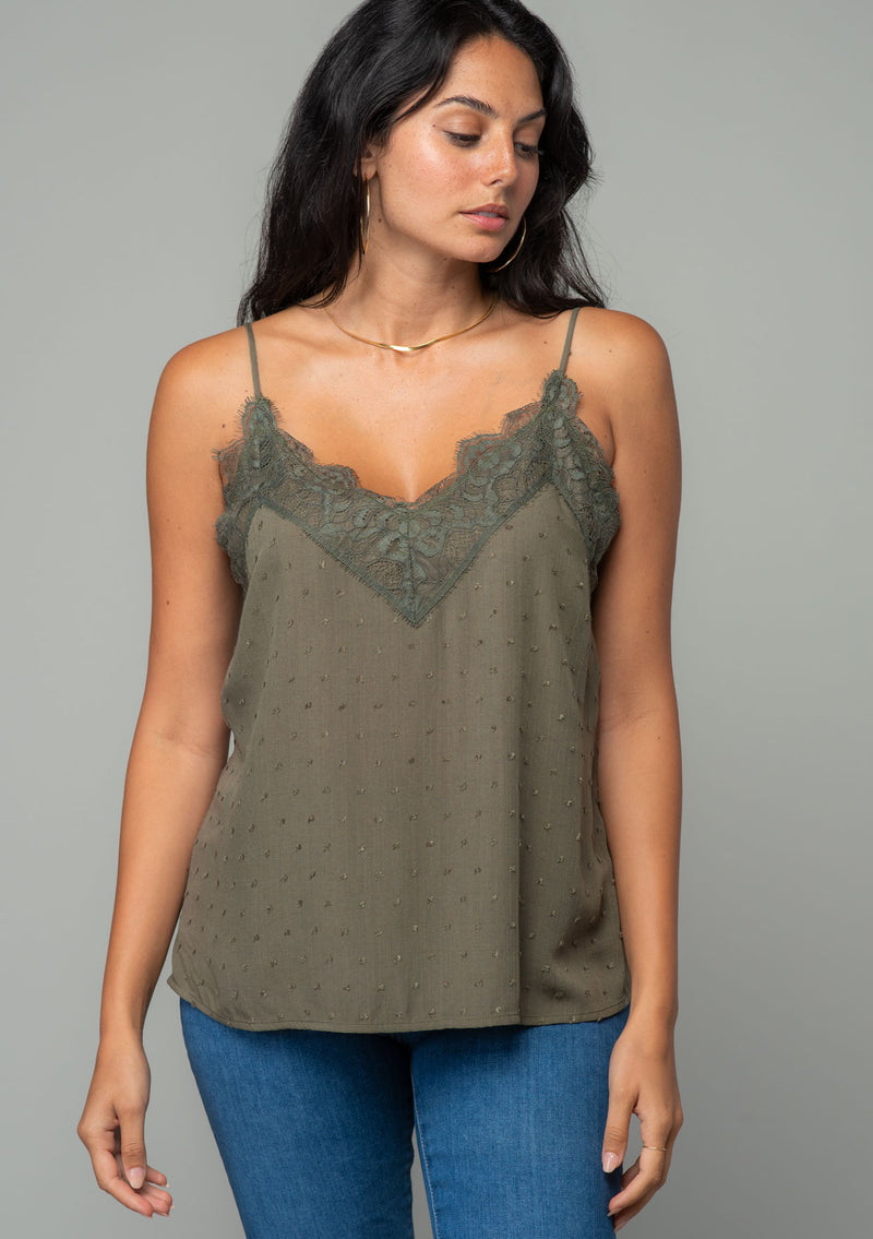 [Color: Olive] A front facing image of a brunette model wearing an olive green clip dot camisole with a lace trim v neckline and adjustable spaghetti straps. The model is wearing gold hoop earrings and a gold necklace.