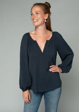 [Color: Charcoal] A half body front facing image of a red headed model wearing a dark grey flowy bohemian peasant top in a textured shadow stripe. With voluminous long sleeves, a split v neckline with hook and eye closure, and a round neckline.