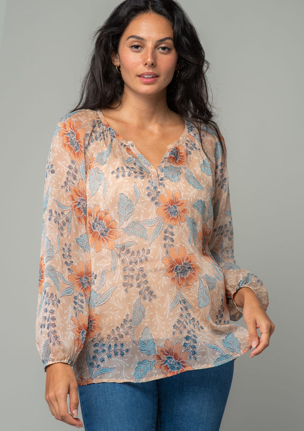 [Color: Coral/Blue] A front facing image of a brunette model wearing a sheer chiffon bohemian blouse in a coral and blue floral print. With long sleeves, a relaxed flowy fit, and a hook and eye closure neckline. 