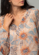 [Color: Coral/Blue] A close up front facing image of a brunette model wearing a sheer chiffon bohemian blouse in a coral and blue floral print. With long sleeves, a relaxed flowy fit, and a hook and eye closure neckline. 