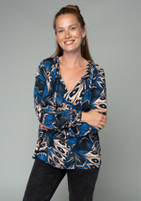 [Color: Cobalt/Tan] A front facing image of a red headed model wearing a bohemian peasant top in a navy blue and tan abstract butterfly wing print. With voluminous long sleeves, a smocked round neckline with tassel ties, and a flowy relaxed fit. 