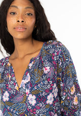 [Color: Navy/Berry] A close up front facing image of a black model with long dark wavy hair wearing a navy blue and berry purple floral print top. With three quarter length sleeves and a v neckline. 