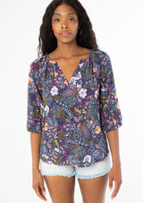 [Color: Navy/Berry] A front facing image of a black model with long dark wavy hair wearing a navy blue and berry purple floral print top. With three quarter length sleeves and a v neckline. 