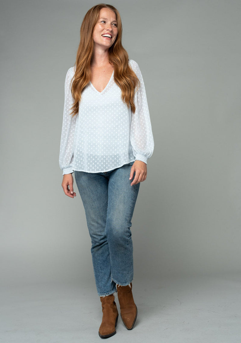 [Color: Ice Blue] A full body front facing image of a red headed model wearing a light blue bohemian blouse in a light catching clip dot sheer chiffon. With voluminous long sleeves, a v neckline, and a relaxed flowy fit. 
