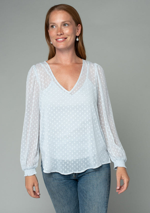 [Color: Ice Blue] A front facing image of a red headed model wearing a light blue bohemian blouse in a light catching clip dot sheer chiffon. With voluminous long sleeves, a v neckline, and a relaxed flowy fit. 