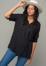 [Color: Black] A front facing image of a brunette model wearing a soft black cotton button front shirt in a textured gingham fabric. With long rolled sleeves, a button front, and a collared neckline.