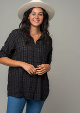 [Color: Black] A front facing image of a brunette model wearing a soft black cotton button front shirt in a textured gingham fabric. With long rolled sleeves, a button front, and a collared neckline. The model is wearing a white bohemian hat. 
