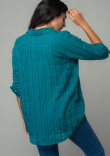 [Color: Teal] A back facing image of a brunette model wearing a soft teal cotton button front shirt in a textured gingham fabric. With long rolled sleeves, a button front, and a collared neckline.