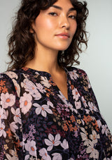 [Color: Black/Dusty Rose] A close up front facing image of a brunette model wearing a sheer chiffon bohemian blouse in a black and rose pink floral print. With long sleeves, ruffled wrist cuffs, and a split v neckline. 
