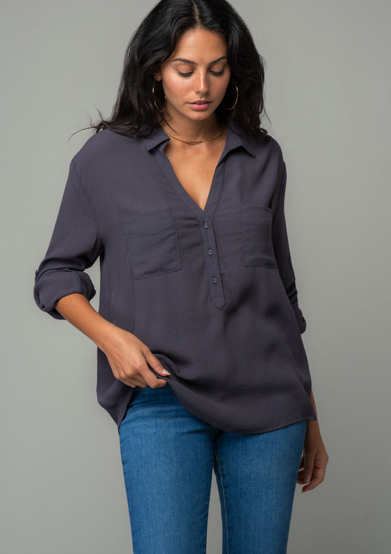 [Color: Charcoal] A front facing image of a brunette model wearing a relaxed fit charcoal grey button front shirt in a lightweight crepe. With long rolled sleeves, a button tab sleeve closure, a front placket, and a collared neckline. 