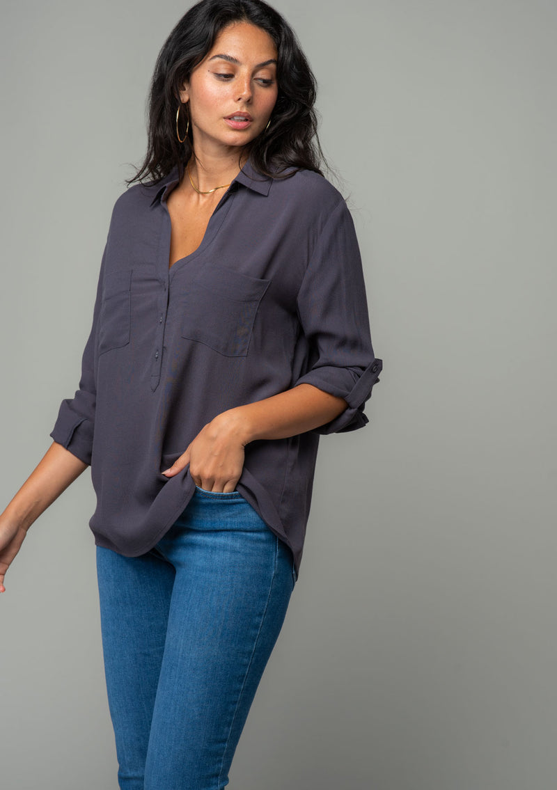 [Color: Charcoal] A half body image of a brunette model wearing a relaxed fit charcoal grey button front shirt in a lightweight crepe. With long rolled sleeves, a button tab sleeve closure, a front placket, and a collared neckline. 
