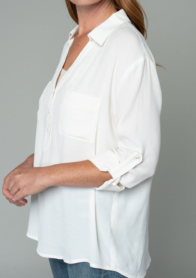 [Color: Gardenia] A close up side facing image of a red headed model wearing a relaxed fit ivory white button front shirt in a lightweight crepe. With long rolled sleeves, a button tab sleeve closure, a front placket, and a collared neckline.