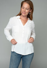 [Color: Gardenia] A half body front facing image of a red headed model wearing a relaxed fit ivory white button front shirt in a lightweight crepe. With long rolled sleeves, a button tab sleeve closure, a front placket, and a collared neckline.