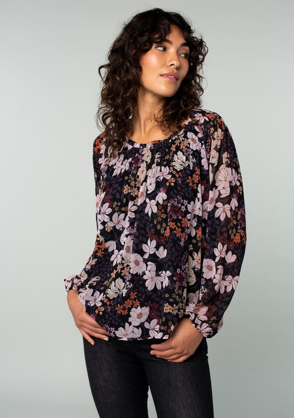 [Color: Black/Dusty Rose] A front facing image of a brunette model wearing a chiffon bohemian blouse in a black and purple floral print. With long sleeves and a smocked elastic round neckline.