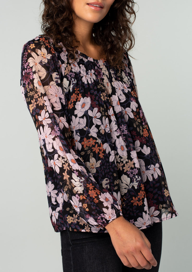 [Color: Black/Dusty Rose] A close up front facing image of a brunette model wearing a chiffon bohemian blouse in a black and purple floral print. With long sleeves and a smocked elastic round neckline.