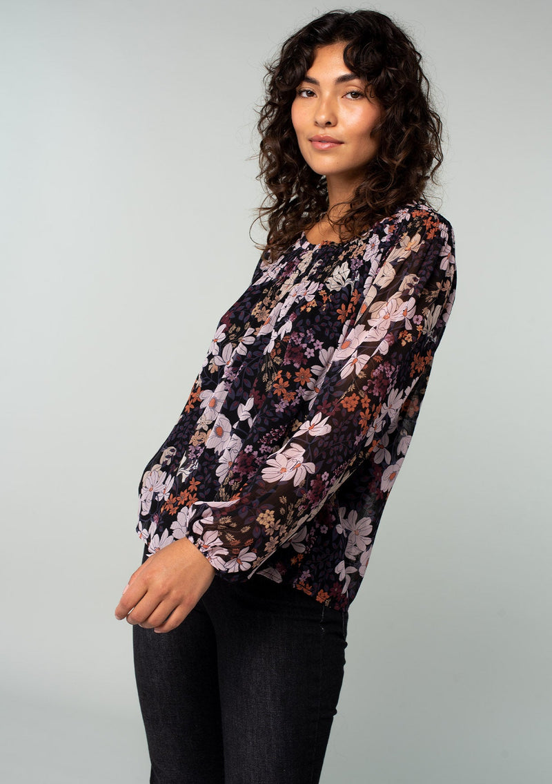 [Color: Black/Dusty Rose] A front facing image of a brunette model wearing a chiffon bohemian blouse in a black and purple floral print. With long sleeves and a smocked elastic round neckline.