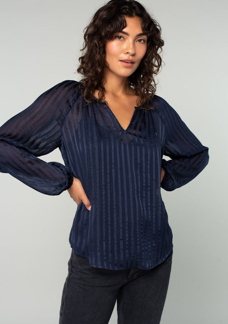 [Color: Navy] A half body front facing image of a brunette model wearing a sheer bohemian navy blue holiday blouse in a sparkly lurex stripe. With voluminous long sleeves and a v neckline. 