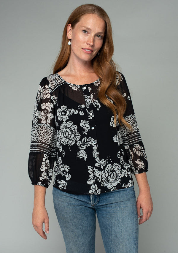 [Color: Black/Cream] A front facing image of a red headed model wearing a bohemian chiffon blouse in a black and cream mixed floral print. With a button front and three quarter length sleeves. 