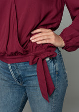 [Color: Wine] A close up front facing image of a red headed model wearing a wine red bohemian holiday top with long sleeves, a faux wrap front, a surplice v neckline, and a side tie detail. 
