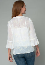 [Color: Ivory] A back facing image of a red headed model wearing an ivory off white holiday blouse in embroidered chiffon. With three quarter length sleeves, a flutter wrist cuff, self covered button front, and a flowy fit. 