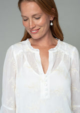 [Color: Ivory] A close up front facing image of a red headed model wearing an ivory off white holiday blouse in embroidered chiffon. With three quarter length sleeves, a flutter wrist cuff, self covered button front, and a flowy fit. 