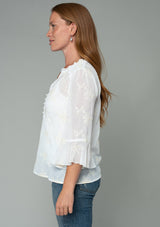 [Color: Ivory] A side facing image of a red headed model wearing an ivory off white holiday blouse in embroidered chiffon. With three quarter length sleeves, a flutter wrist cuff, self covered button front, and a flowy fit. 