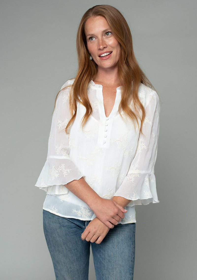 [Color: Ivory] A front facing image of a red headed model wearing an ivory off white holiday blouse in embroidered chiffon. With three quarter length sleeves, a flutter wrist cuff, self covered button front, and a flowy fit. 