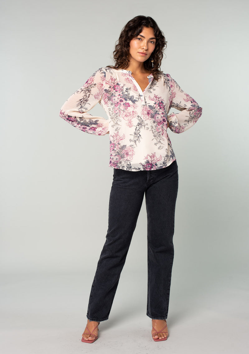 [Color: Natural/Wine] A full body front facing image of a brunette model wearing a sheer chiffon bohemian blouse in a natural and wine purple floral print. With a front placket, long voluminous sleeves, and a flowy relaxed fit. 