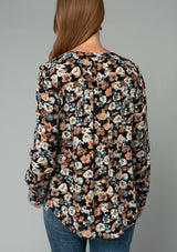 [Color: Black/Natural] A back facing image of a red headed model wearing a lightweight long sleeve top in a black and natural floral print. With a split v neckline and a relaxed flowy fit. 