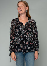 [Color: Black/Dusty Rose] A front facing image of a red headed model wearing a bohemian chiffon blouse in a black and pink floral print. With voluminous long sleeves, adjustable wrist ties, and a self covered button front. 