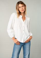 [Color: White] A front facing image of a blonde model wearing a classic bohemian cotton white button front shirt in a textured jacquard. With long sleeves and a ruffled neckline.