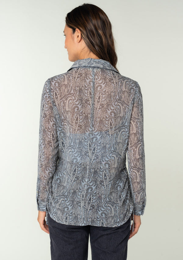 [Color: Grey/Natural] A back facing image of a brunette model wearing a sheer chiffon button front shirt in a grey and natural paisley print. With a collared neckline, long sleeves with a button wrist cuff, and an adjustable side gathered waist detail with ties. 