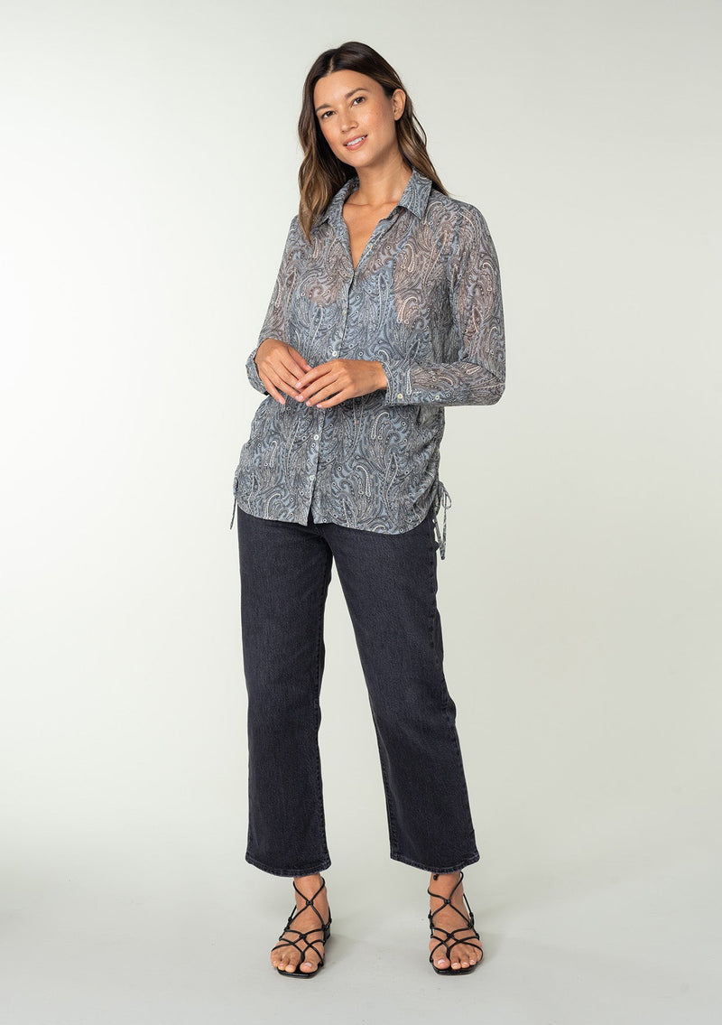 [Color: Grey/Natural] A full body front facing image of a brunette model wearing a sheer chiffon button front shirt in a grey and natural paisley print. With a collared neckline, long sleeves with a button wrist cuff, and an adjustable side gathered waist detail with ties. 
