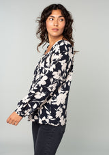 [Color: Black/Natural] A side facing image of a brunette model wearing a black and off white floral print blouse. A bohemian resort top with long sleeves and a wide elastic neckline. 