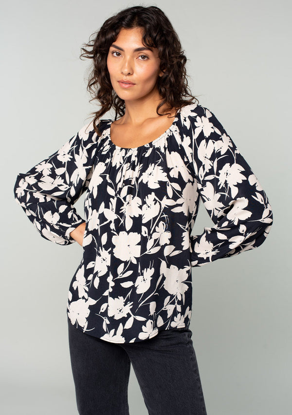 [Color: Black/Natural] A front facing image of a brunette model wearing a black and off white floral print blouse. A bohemian resort top with long sleeves and a wide elastic neckline. 