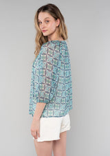 [Color: Cream/Navy] A side facing image of a blonde model wearing a sheer chiffon bohemian blouse in a blue floral geometric print. With three quarter length sleeves and a split neckline with ties. 
