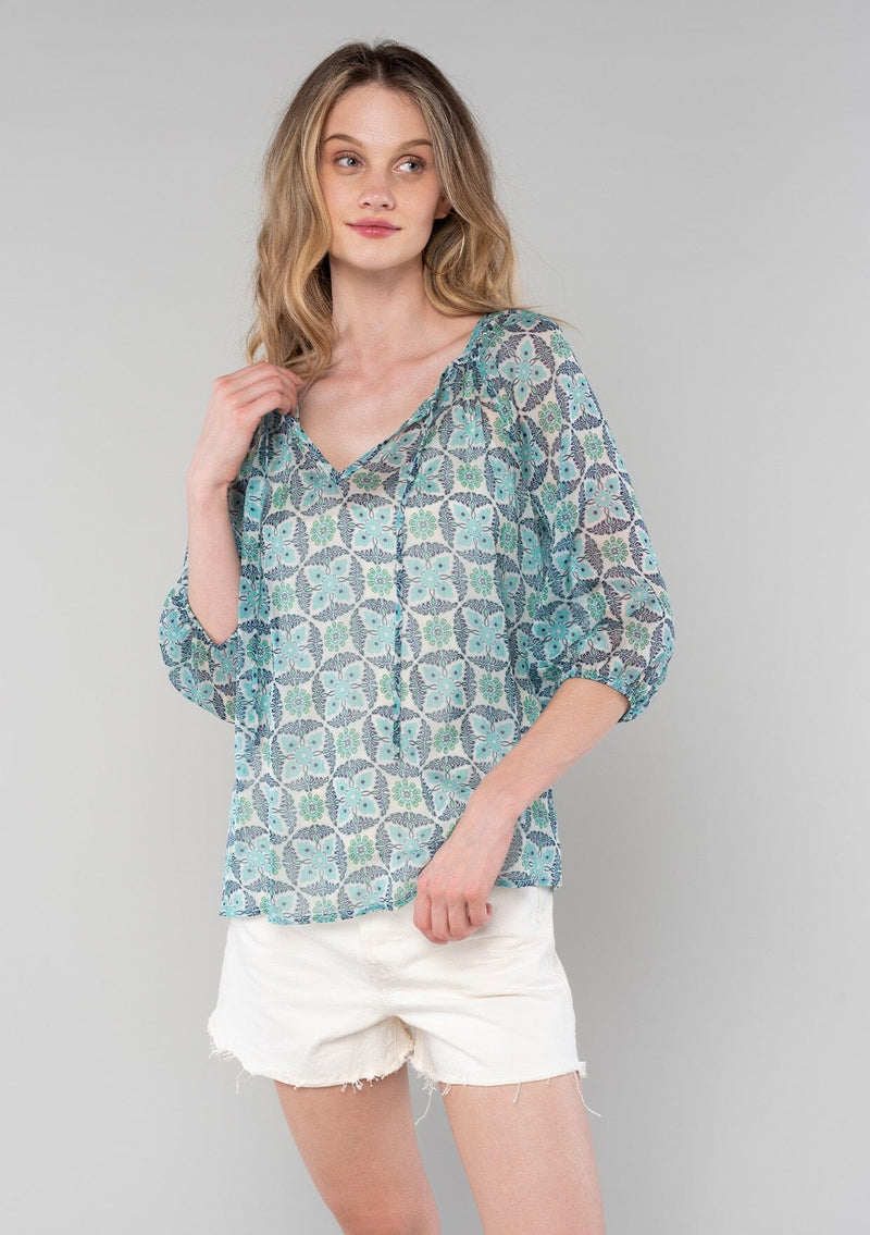 [Color: Cream/Navy] A front facing image of a blonde model wearing a sheer chiffon bohemian blouse in a blue floral geometric print. With three quarter length sleeves and a split neckline with ties. 