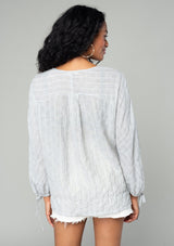 [Color: Heather Grey] A back facing image of a brunette model wearing a sheer cotton bohemian top in a heather grey striped jacquard. With long sleeves, a button front, and tie wrist cuffs.