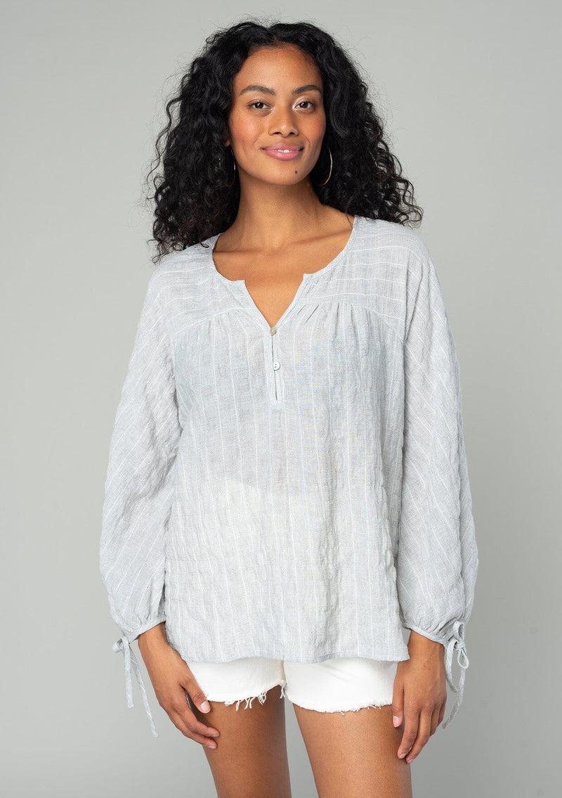 [Color: Heather Grey] A front facing image of a brunette model wearing a sheer cotton bohemian top in a heather grey striped jacquard. With long sleeves, a button front, and tie wrist cuffs.