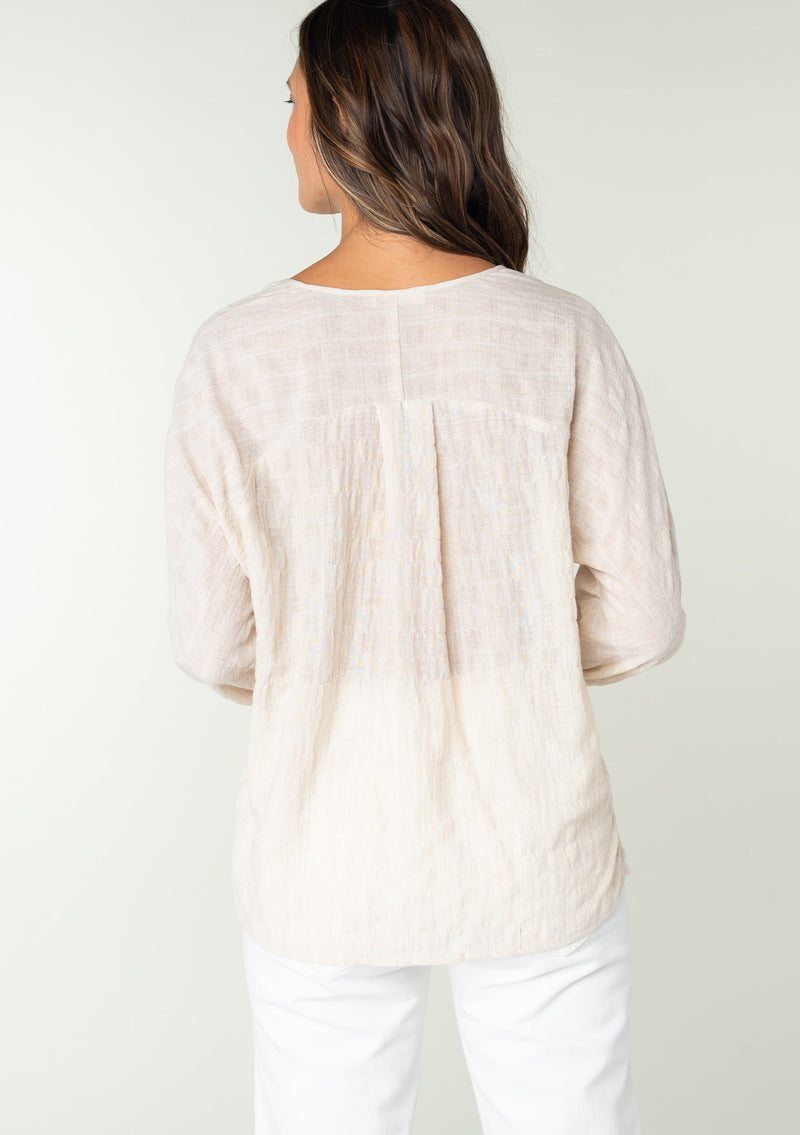 [Color: Oatmeal] A back facing image of a brunette model wearing a sheer cotton bohemian top in a striped jacquard. With long sleeves, a button front, and tie wrist cuffs. 