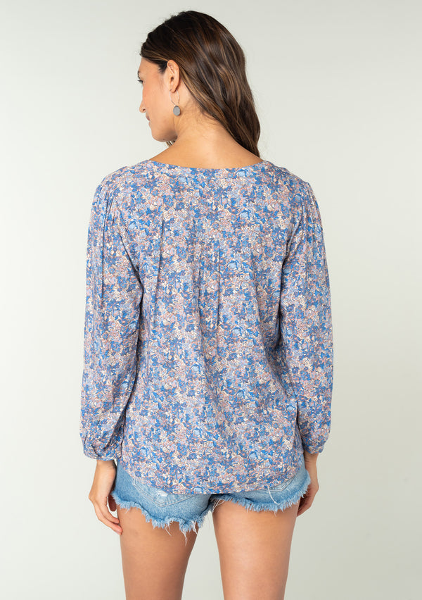 [Color: Blue/Coral] A back facing image of a brunette model wearing a blue and coral floral print bohemian blouse. With long sleeves and a button front. 