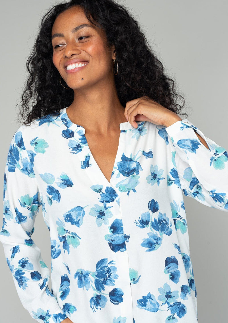 [Color: Ivory/Aqua] A close up front facing image of a brunette model wearing a classic long sleeve blouse in an ivory white and blue floral print. With a v neckline and button wrist cuff. 