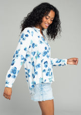 [Color: Ivory/Aqua] A side facing image of a brunette model wearing a classic long sleeve blouse in an ivory white and blue floral print. With a v neckline and button wrist cuff. 