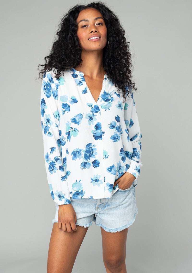 [Color: Ivory/Aqua] A front facing image of a brunette model wearing a classic long sleeve blouse in an ivory white and blue floral print. With a v neckline and button wrist cuff. 