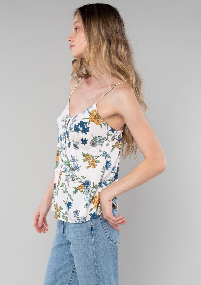 [Color: Natural/Mustard] A side facing image of a blonde model wearing a sexy bohemian tank top in a blue and yellow floral print. A spring camisole with a self covered button front, a v neckline, and adjustable spaghetti straps. 