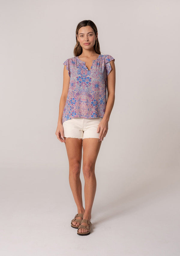 [Color: Dusty Rose/Blue] A front facing image of a brunette model wearing a lightweight summer top in a pink and blue floral print with light catching gold metallic clip dot details. With short ruffle sleeves and a v neckline. 