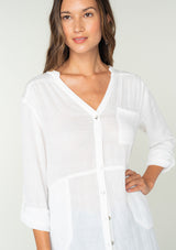 [Color: White] A close up front facing image of a brunette model wearing a classic lightweight white tunic shirt. With long sleeves, a button tab sleeve, a button front, a v neckline, and side pockets. 